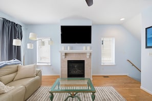 A living room with a sofa, a glass coffee table, a fireplace, a flat-screen TV, and a staircase.