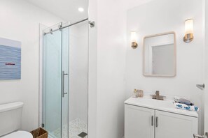 Ein Badezimmer mit Duschkabine aus Glas, einem weißen Waschbecken mit Spiegel und einer Toilette.