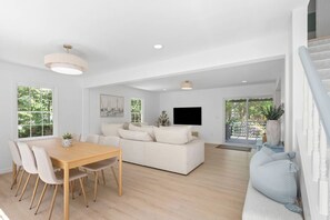 A spacious living area with a dining table, sofa, and a TV mounted on the wall.