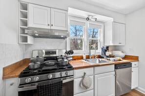 A modern kitchen with white cabinets, a stainless steel stove, a dishwasher, and a window providing natural light.