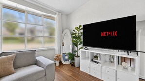 Una sala de estar moderna con un sofá gris, un mueble blanco para el entretenimiento y un televisor de pantalla plana grande que muestra el logo de Netflix.