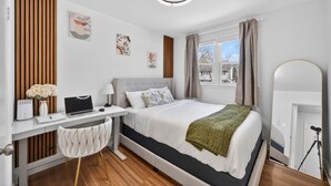 Un dormitorio moderno con cama, escritorio, silla y espejo.