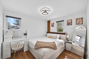 A bedroom with a bed, bedside tables, a vanity with a mirror, and a window.