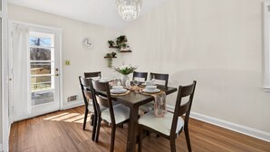 Comedor con una mesa de madera dispuesta para seis comensales, rodeada de sillas, una araña y estanterías murales con plantas.