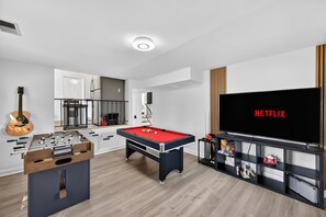 A modern living room with a foosball table, pool table, and a large TV screen displaying 'NETFLIX'.