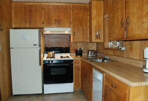 Een keuken met houten kastjes, een koelkast, een oven, een vaatwasser en een spoelbak.