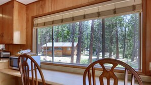 Eine Küche mit Holzschränken, einer Mikrowelle und einem großen Fenster mit Blick auf einen Wald.