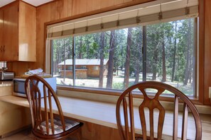 A kitchen with wooden cabinets, a microwave, and a large window overlooking a forest. - (37A) Alpine - The Redwoods in Yosemite (Yosemite National Park)