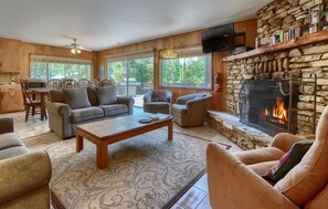 A cozy living room with a stone fireplace, comfortable seating, a flat-screen TV, and large windows. - (37A) Alpine - The Redwoods in Yosemite (Yosemite National Park)