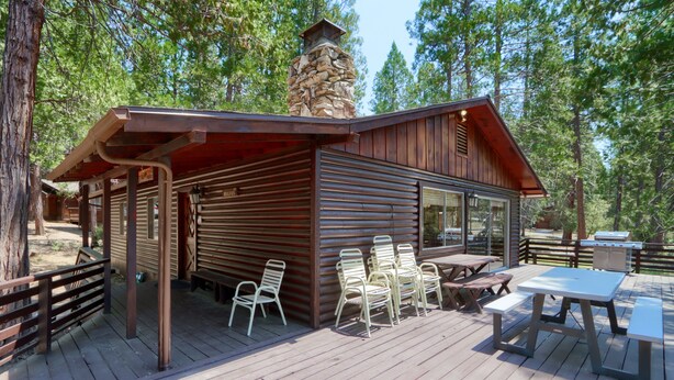 Eine Holzhütte mit einer Veranda, Sitzgelegenheiten im Freien und einem Steinkamin.