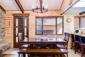 A wooden interior with a dining table, chairs, a chandelier, a stone wall, and a door with a sign. - (42A) Megan's Retreat at The Redwoods in Yosemite (Yosemite National Park)