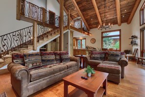 A spacious living area with a wooden staircase, leather sofas with patterned cushions, a wooden coffee table, and a large window providing natural light. - Yosemite's Grand Estate - Private Estate for Large Gatherings (Yosemite National Park)