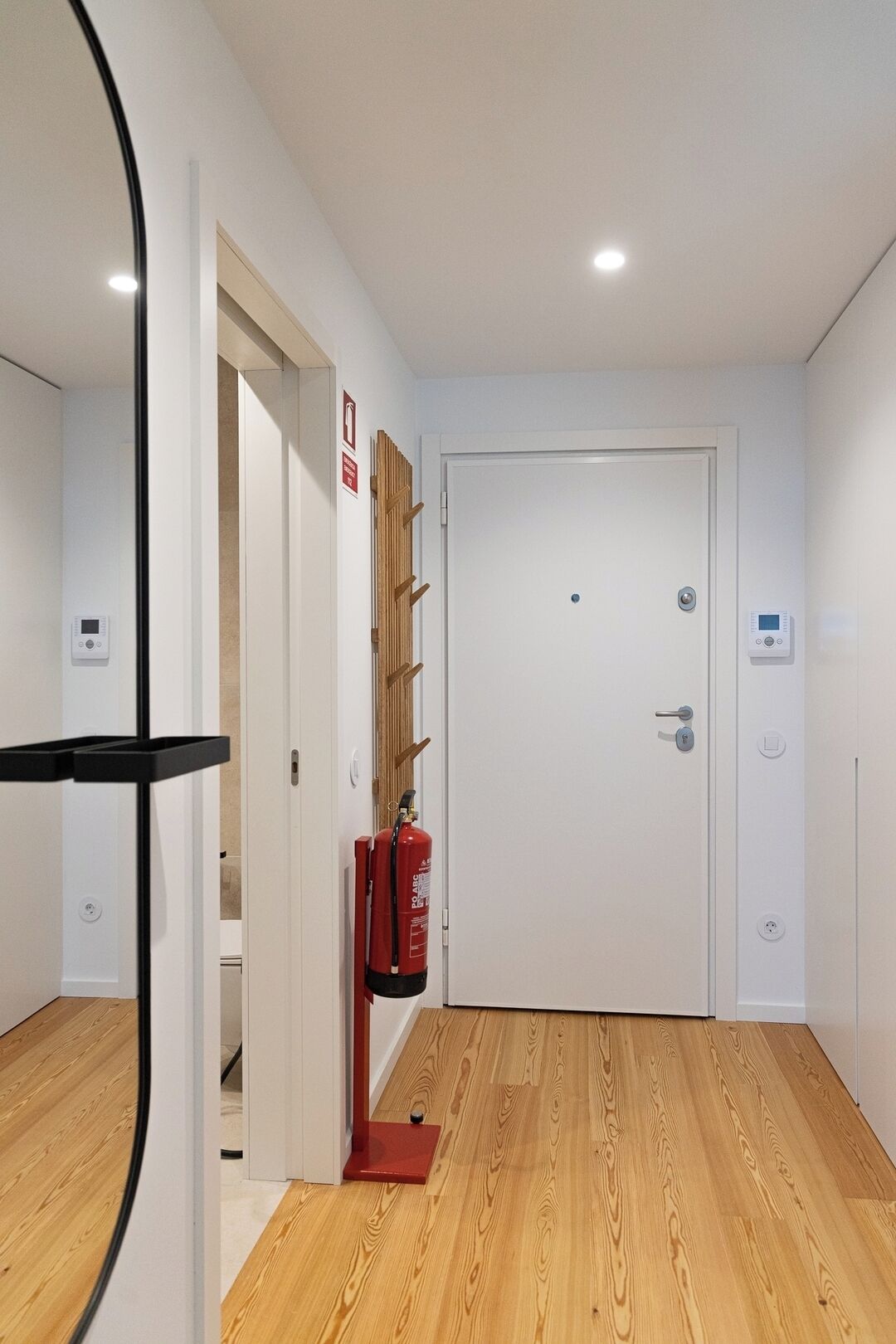 A hallway with a wooden floor, a white door, and a fire extinguisher mounted on the wall.