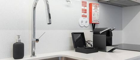 A modern kitchen with a stainless steel sink, a faucet, a soap dispenser, a coffee machine, and a fire safety poster.