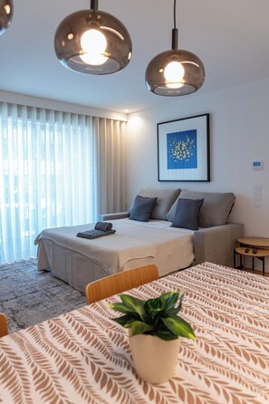 A modern bedroom with a bed, a sofa, a dining table with a plant, and a ceiling light fixture. - Sal Douro Golden | Sea View and Comfort (Vila Nova de Gaia)