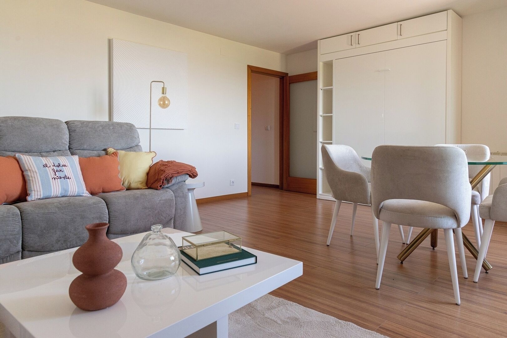 A modern living room with a grey sofa, a white coffee table, and a dining area with white chairs.