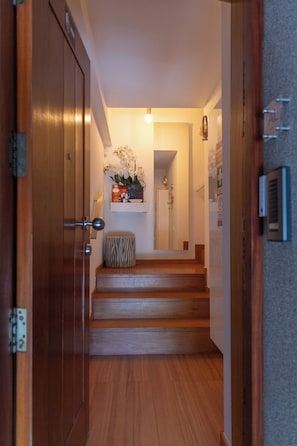 A wooden staircase leading to a room with a white door, a small bench, and a shelf with flowers and a vase. - Blue Frame | Ocean front (Vila Nova de Gaia)
