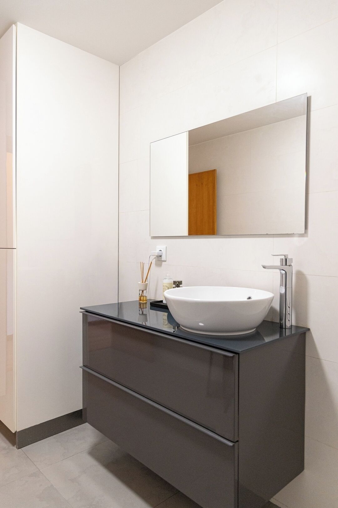 A modern bathroom with a white sink, dark cabinetry, and a large mirror.