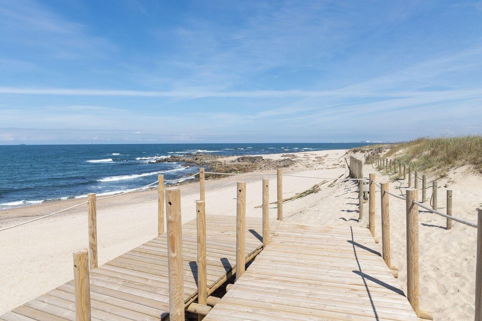 A wooden boardwalk leading to a beach with a clear view of the ocean and distant shoreline.