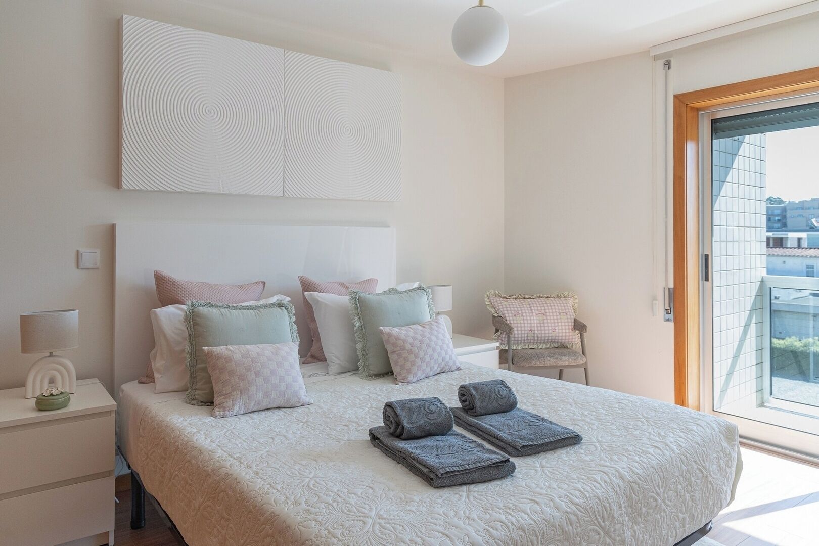 Ein Schlafzimmer mit einem großen Bett, Nachttischen, einem Sessel und Blick durch ein Fenster.