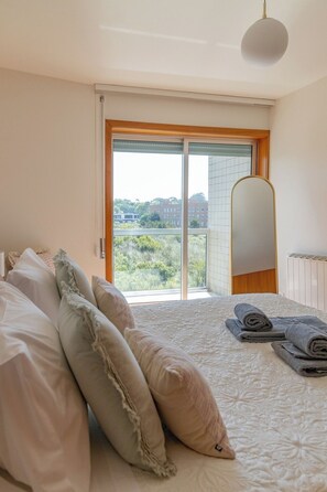 A bedroom with a bed, pillows, a view through a sliding door, and a radiator. - Blue Frame | Ocean front (Vila Nova de Gaia)