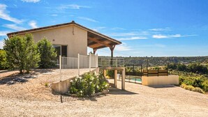 Et moderne hus med en overdækket terrasse, en swimmingpool og udsigt over det omkringliggende landskab.