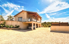 A two-story house with a balcony, a car parked in the driveway, and a gravel ground. - Beautiful home in Gras (Gras)
