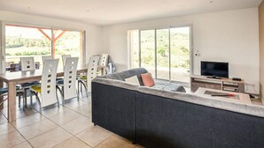En moderne stue med en stor sofa, et spiseområde med stole, et fjernsyn og en balkon med udsigt.