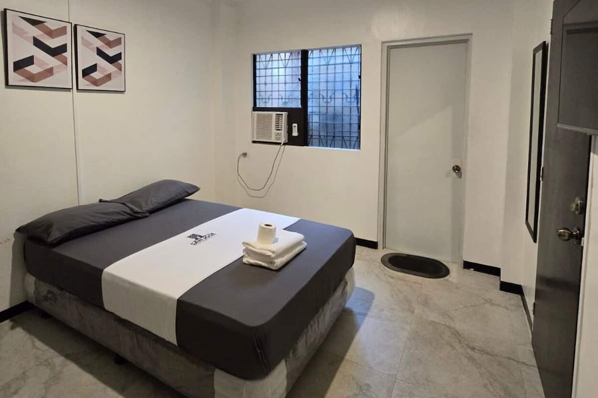 Ein Schlafzimmer mit Bett, einem Fenster mit Gitterstäben, einer Klimaanlage und einer Tür.