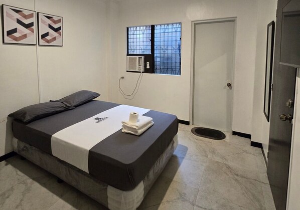 A bedroom with a bed, a window with bars, an air conditioning unit, and a door. - San Jose Pension House by Hiverooms (Cebu City)