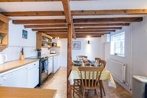 A kitchen with wooden beams, a dining table with chairs, and a window. - The Cottage at Homeleigh, Southwold (Southwold)