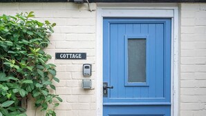 En blå dörr med ett litet fönster, en skylt med texten ”COTTAGE” och en säkerhetsanordning på väggen.