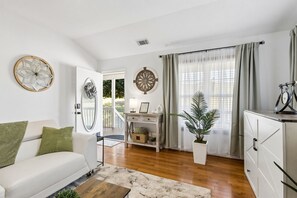 Ein modernes Wohnzimmer mit einem weißen Sofa, einem Couchtisch, einer Topfpflanze, einem Schreibtisch mit Lampe und einem Fahrrad auf einem Schrank.