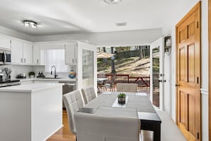 Eine moderne Küche mit weißen Schränken, ein Essbereich mit Tisch und Stühlen sowie ein Blick auf einen Hinterhof mit einer Holzterrasse und Gartenmöbeln.