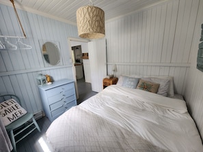 Une chambre à coucher comprenant un lit, une commode, un miroir et un luminaire suspendu.