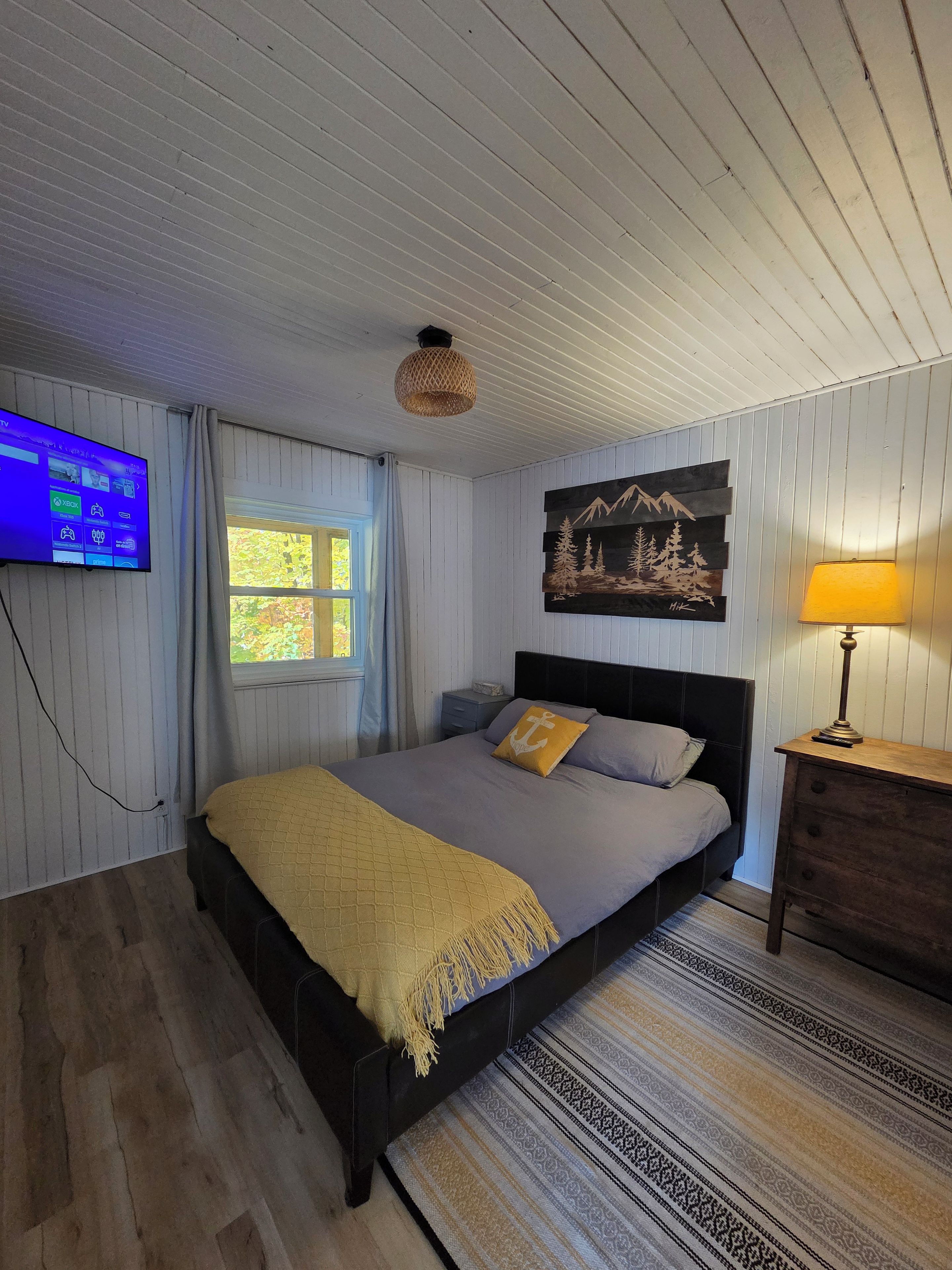 Une chambre à coucher avec un lit, une table de chevet, une lampe, un tableau et un téléviseur fixé au mur.