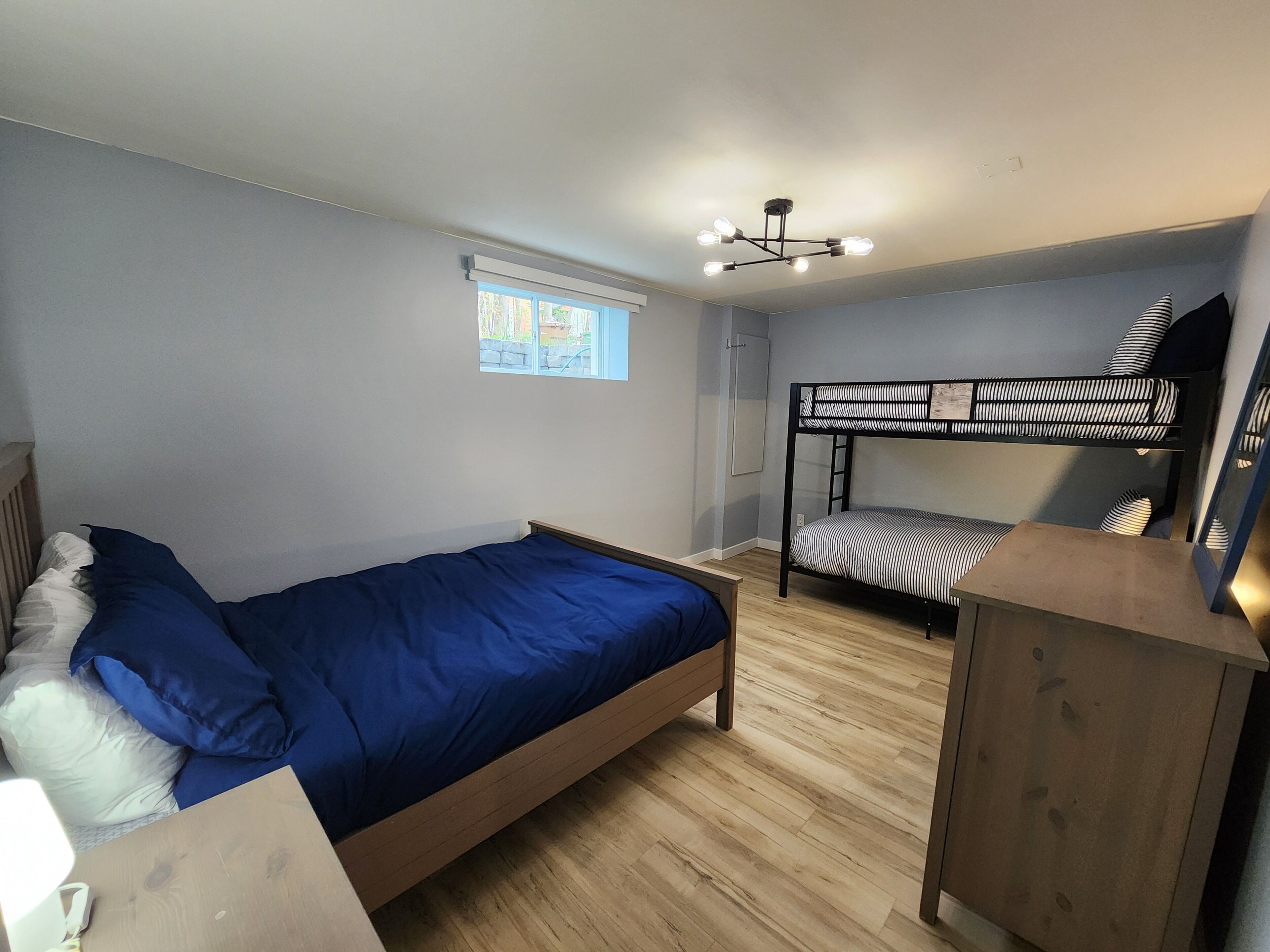 A bedroom with a single bed, a bunk bed, a wooden dresser, and a ceiling light fixture.