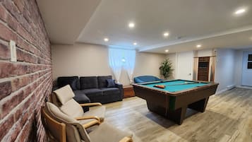 Una habitación con mesa de billar, un sofá, una silla, una pared de ladrillo y una puerta.