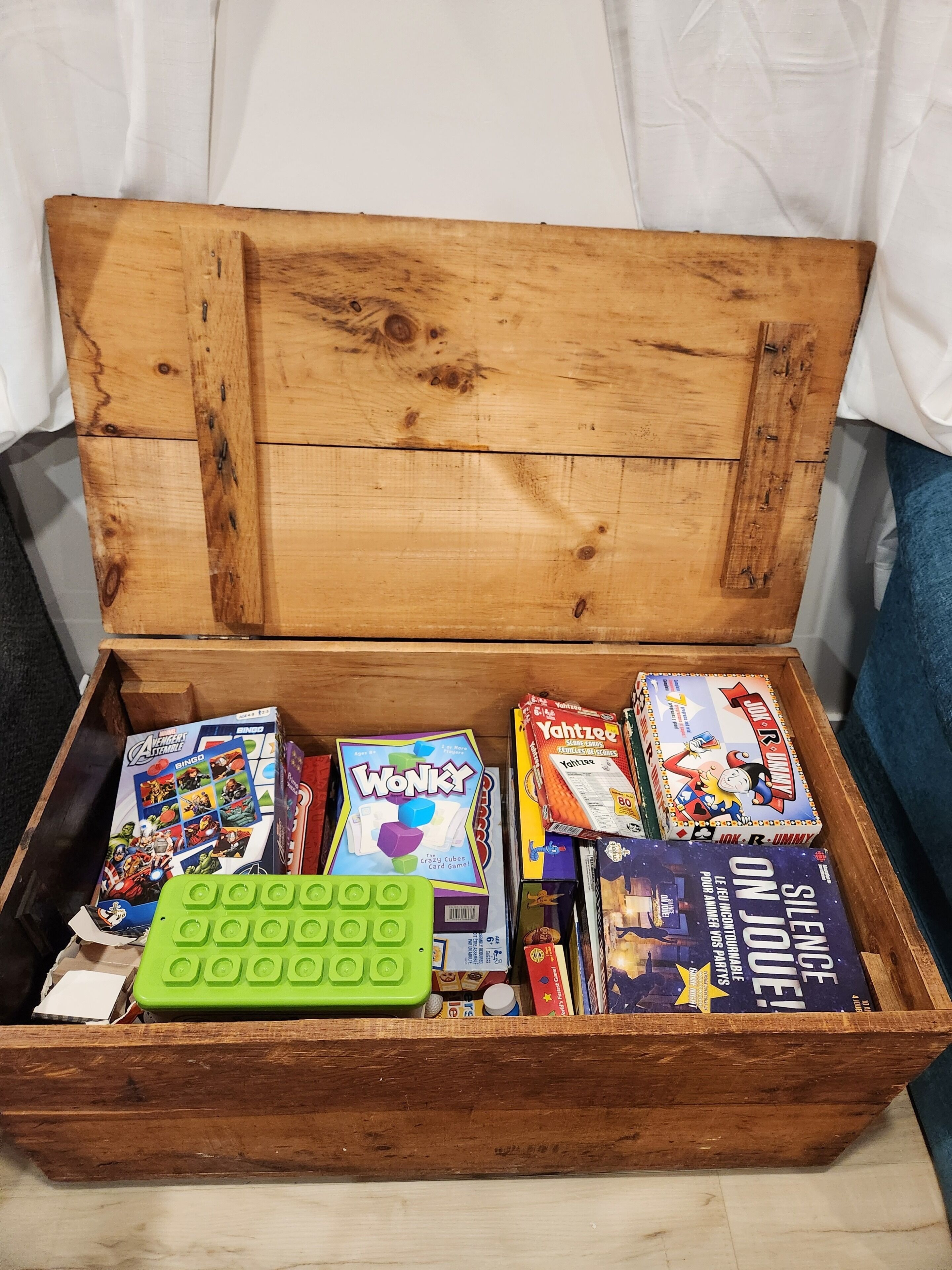 A wooden chest filled with various board games and a green game cube.