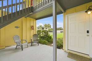 A yellow building with a white door, two Adirondack chairs, a fire extinguisher, and a staircase leading to an upper level. - Beach Bungalow - Walk to the Beach/Pool steps away (St. Augustine)
