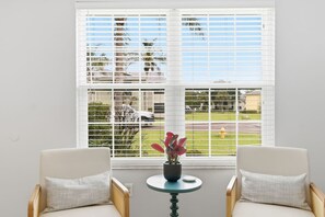 Ein Zimmer mit einem großen Fenster, zwei Stühlen, einem kleinen Tisch und einer Topfpflanze.