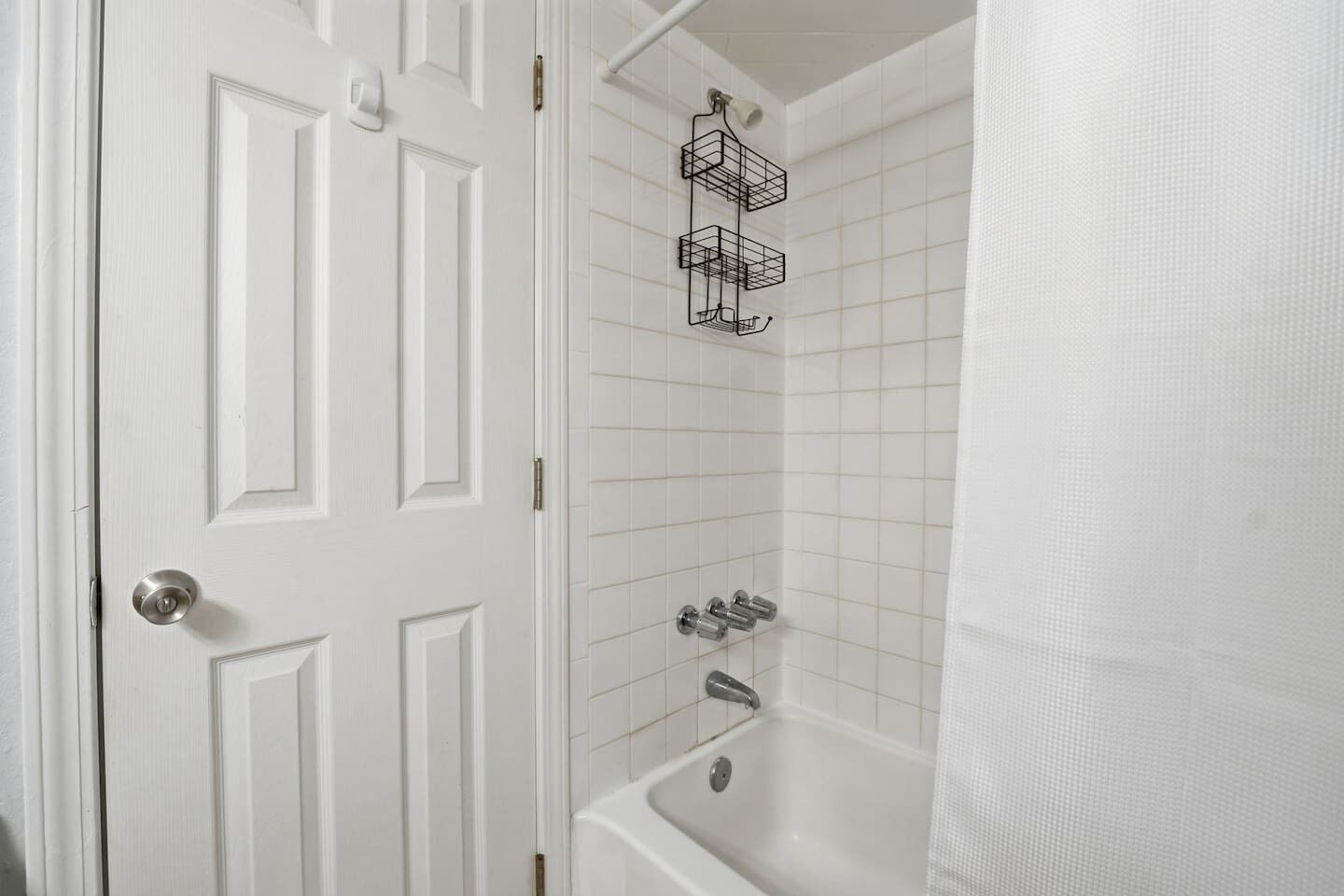 A white bathroom with a bathtub, a shower, and a door with a silver handle.