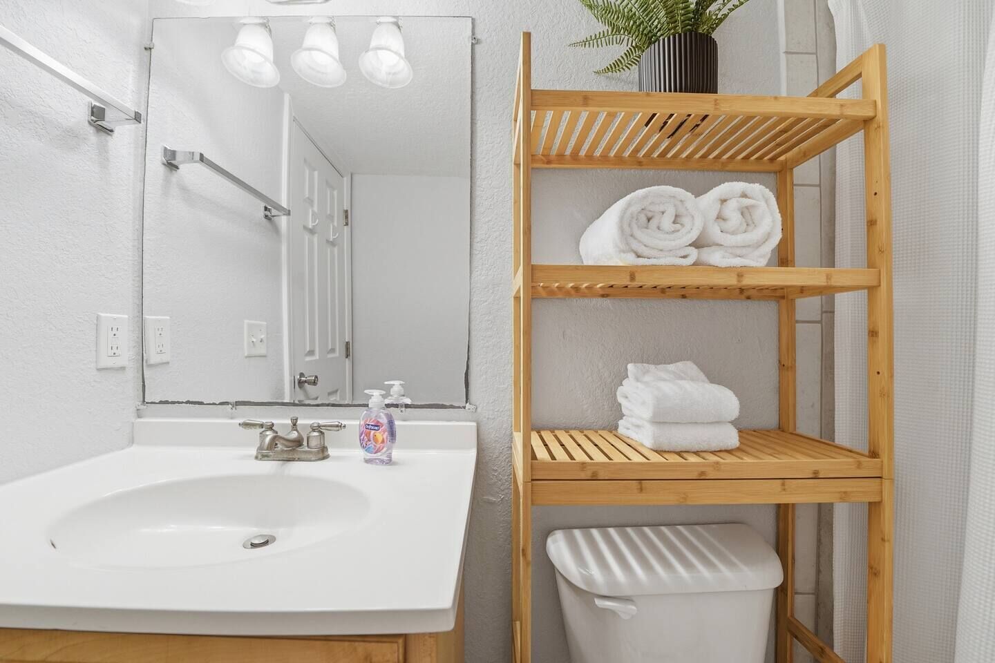 A bathroom with a white sink, mirror, and wooden shelf holding towels.