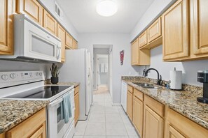 A kitchen with wooden cabinets, a microwave, a stove, a sink, and a coffee maker. - Beach Bungalow - Walk to the Beach/Pool steps away (St. Augustine)