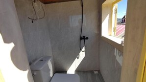 Un baño pequeño y estrecho con inodoro, ducha y ventana.