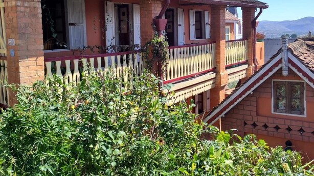 Una casa de dos pisos con balcón, paredes de ladrillo y techo de tejas.