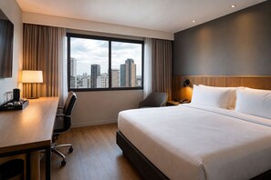 A hotel room with a large bed, a desk with a lamp, a chair, a bedside table with a phone, and a view of the cityscape through the window. - Brazil CNPJ Test II - numeric (São Paulo)