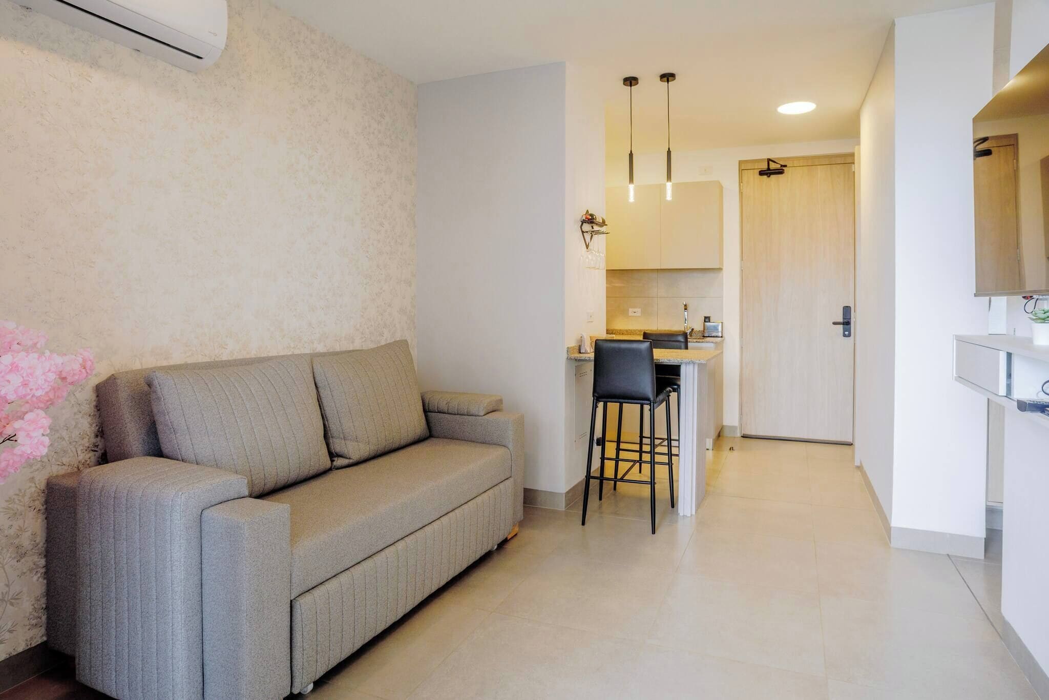 A modern living room with a sofa, a dining area with a chair, and a kitchen in the background.