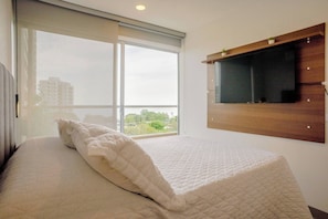 A bedroom with a bed, a window with a view, and a mounted TV. - Modern Beachfront Loft in Santa Marta (Santa Marta)