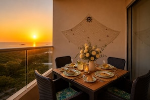 Mesa de jantar com pratos, copos e uma vela, com vista para o pôr do sol.